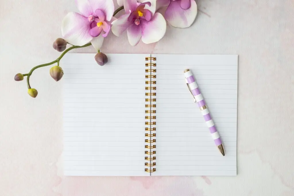 Flat‑lay of notebook with pink pen and pink orchid