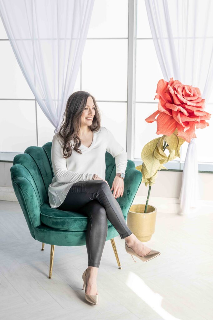 Personal branding portrait of a woman seated on a green velvet chair beside oversized paper flowers — photographed by Marta Raptis in Mississauga studio.