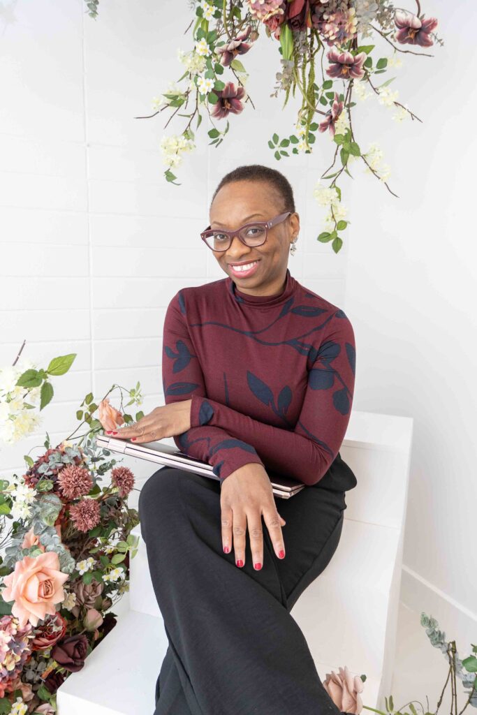 Joanna Aborhey smiling while seated with notebook and flowers, sharing her experience from a relaxed branding photo session with Marta Raptis.