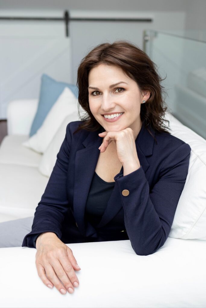 Professional branding photo of Erin smiling in a navy blazer on a white sofa — modern, approachable portrait captured in Oakville.