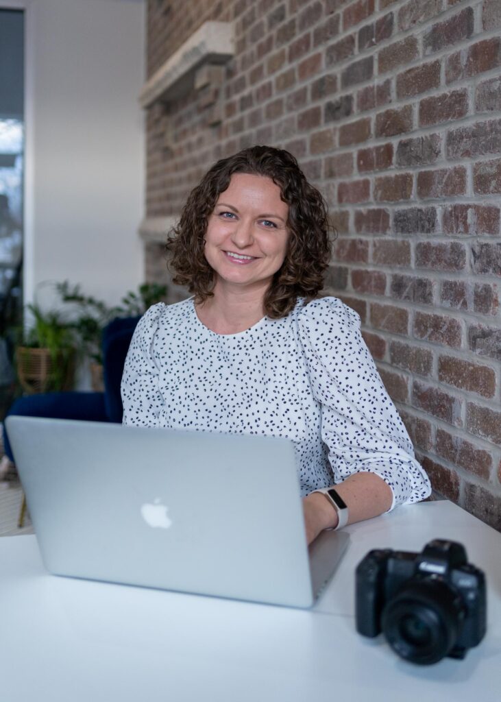 Marta Raptis sitting at a desk smiling with laptop and camera
