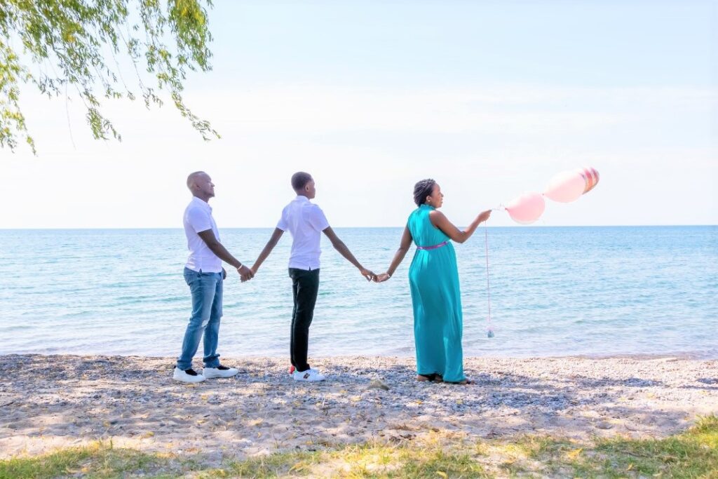Family portrait of three people holding hands on a lakeshore with pink balloons — photographed by Marta Raptis in Mississauga.
