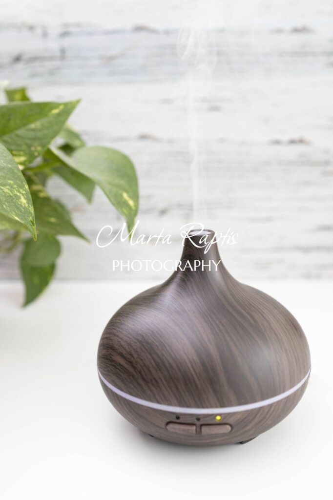Dark essential oil diffuser releasing mist beside green leaves, soothing aromatherapy stock image.