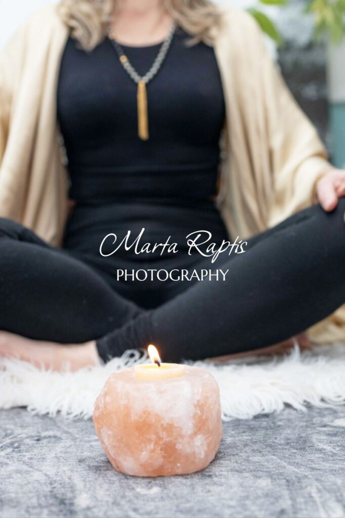 Woman sitting cross‑legged in meditation pose with plant nearby, calming wellness stock image.