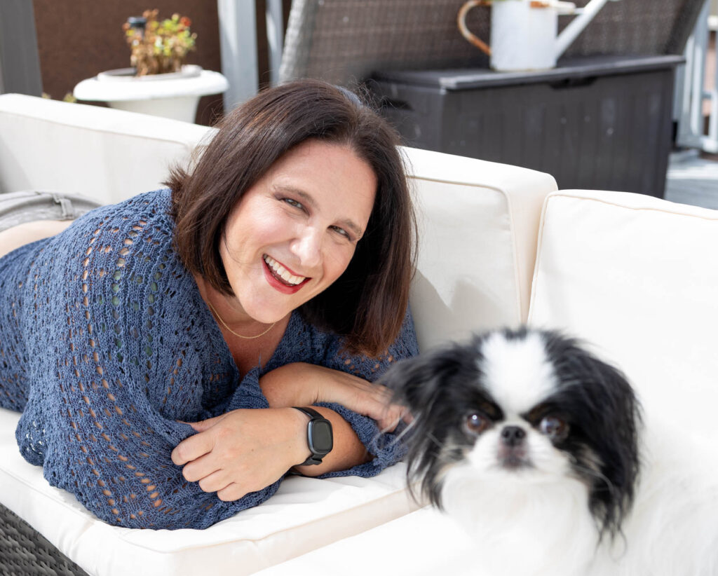 Woman sitting on a couch smiling beside her black‑and‑white dog, photographed for Marta Raptis Photography branding session — a warm, authentic moment representing genuine connection and personality in marketing.