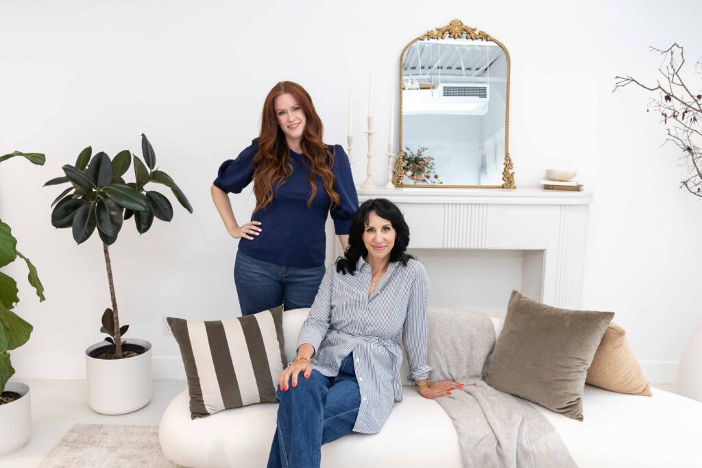 Samara Foisy and Allison Jorgens posing together on sofa with neutral decor, photographed for Qwiky Wellness branding shoot by Marta Raptis.