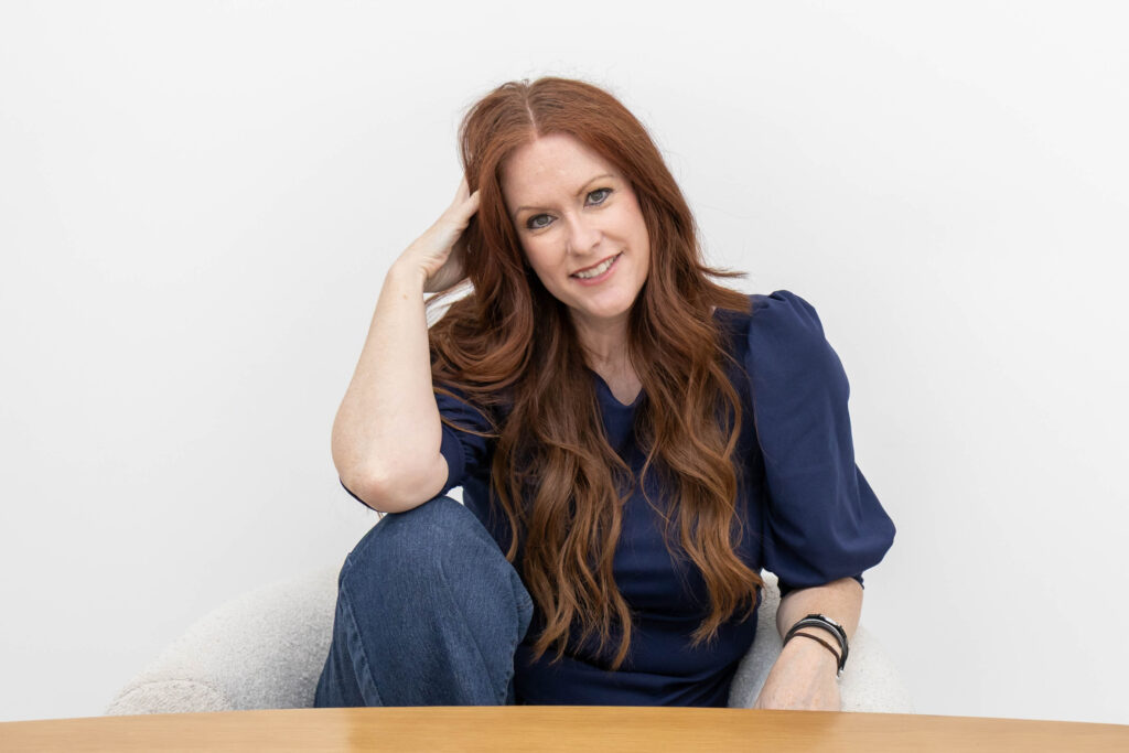 Allison Jorgens seated casually with hand resting on her head, wearing a navy blouse and jeans, photographed for Qwiky Wellness branding shoot by Marta Raptis.