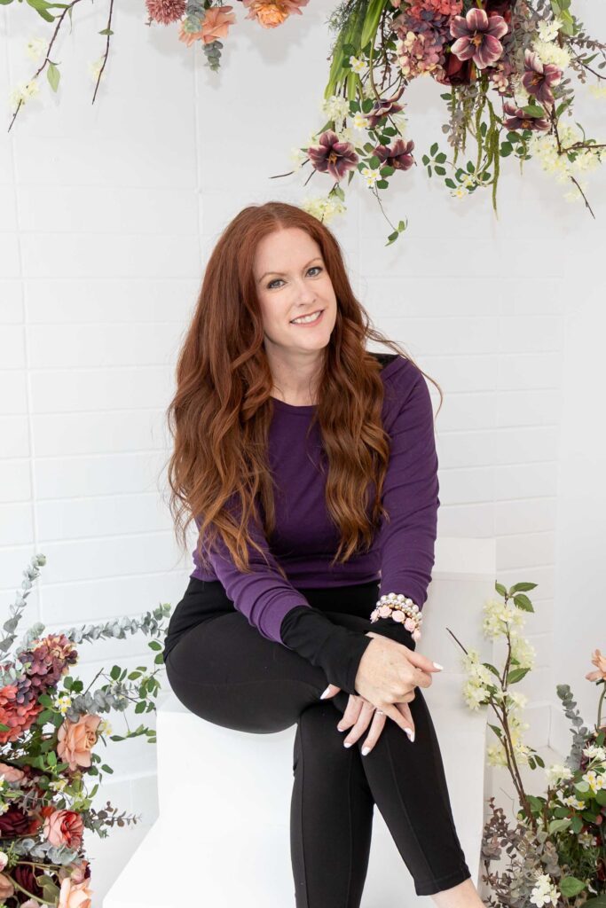 Allison Jorgens seated in purple top with floral backdrop, photographed for Qwiky Wellness branding shoot by Marta Raptis.