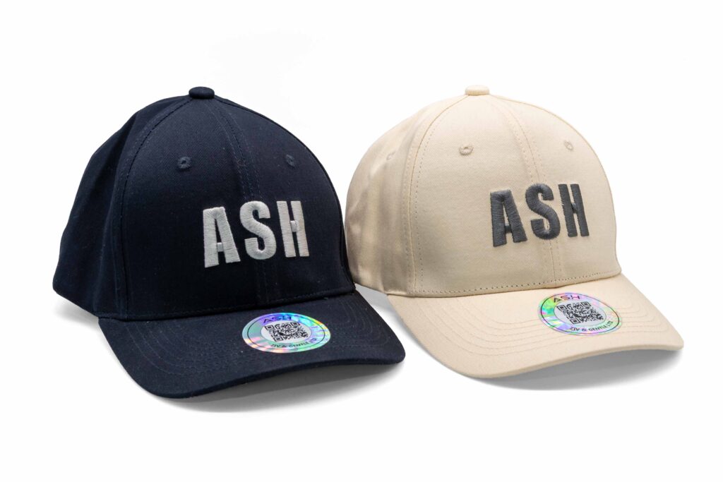 Beige and black ASH baseball caps side by side, highlighting color variations and logo embroidery.