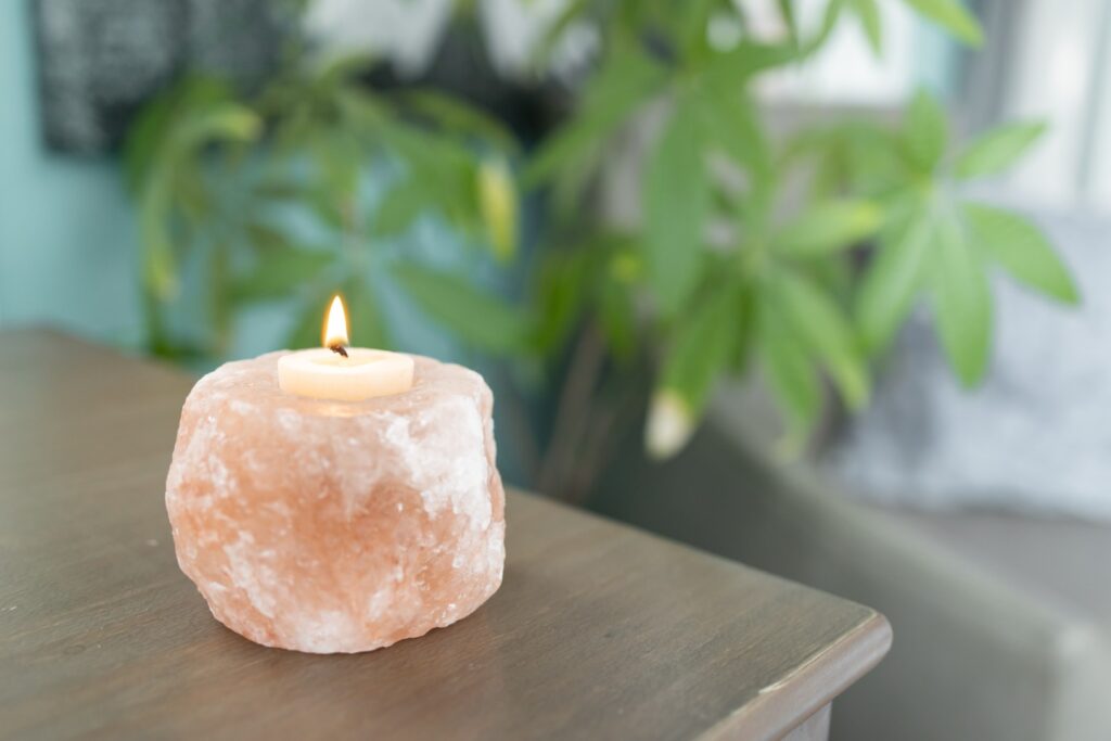 Himalayan salt candle holder glowing softly on wooden table with green plant blurred in background, creating a calm, natural ambiance.